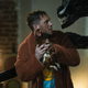 Tom Hardy staring at Venom the symbiote while holding a chicken.